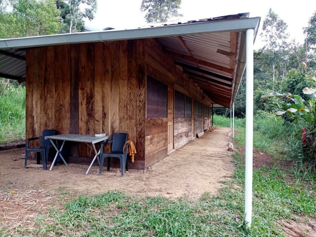 Photo of a long wooden structure with many doors. The side of the structure is short, and has two chairs next to a small table.