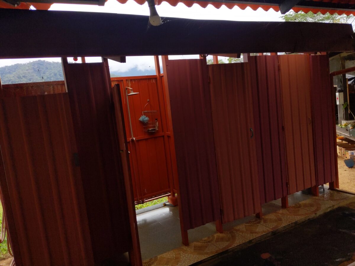 Four red metal shower stalls with the lush jungle hillsides in the background