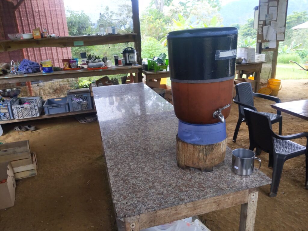 Photo of a small tank with a water tap in the side and a metal cup next to it