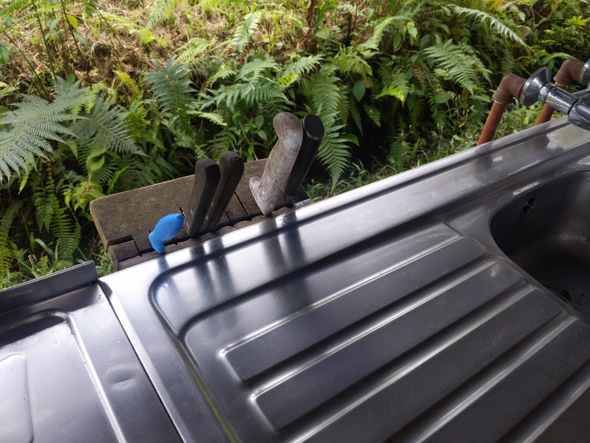 Photo of a wooden block holding 5 knives next to a steel sink