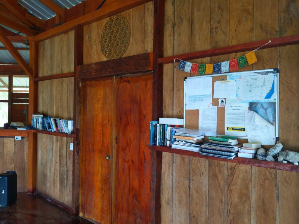 Photo of a doorway with two bookshelves on either side. Above the doorway is a Seed of Life. Next to the bookshelf on the right are various crystals, Nepali prayer flags, and a cork board with several information papers on it.