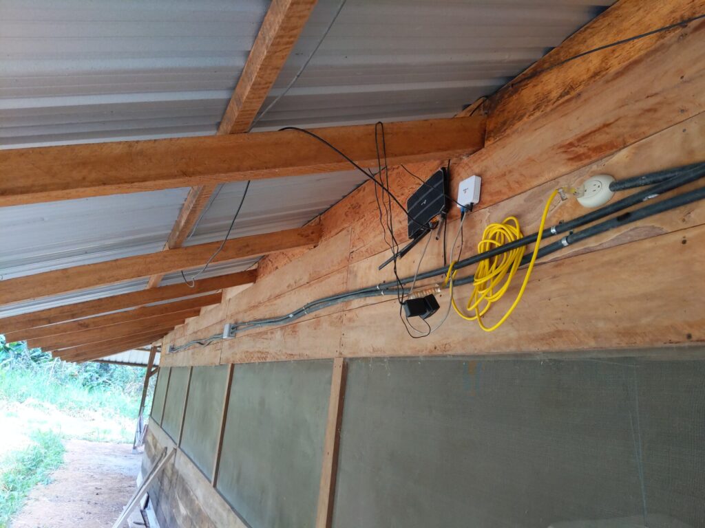 Photo of a black access point branded "tp-link" next to a fiber switch. Both are mounted on the exterior wall of a long wooden structure.