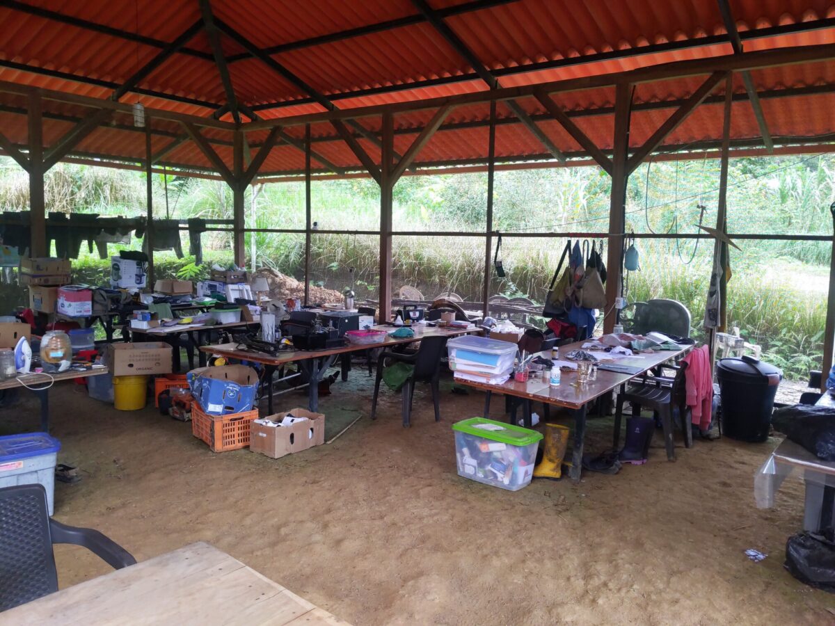 Photo shows 6 tables. Some of the tables have laptops on them. They are also cluttered with many other items, including various pieces of electronics in various states of disrepair.