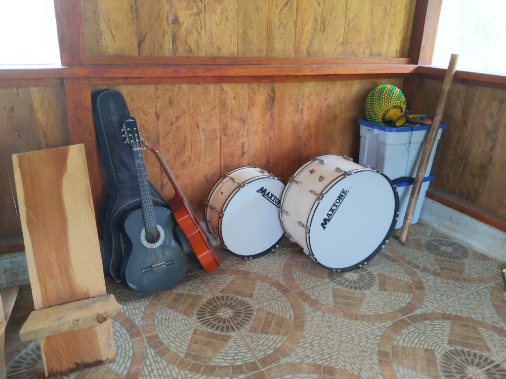 Photo shows a guitar case, two guitars, two large drums, a colorful xylophone, and a bamboo pole