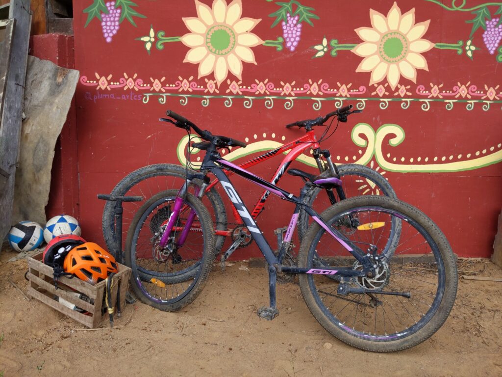Photo shows two mountain bicycles, a wooden crate with helmets, a volleyball, and a football